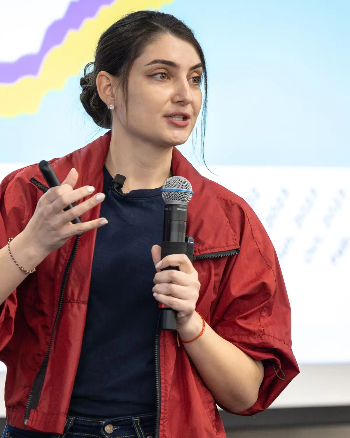 Katie Gamanji speaks on stage at KCD Texas 2026, holding a microphone in front of a slide with a rising chart.